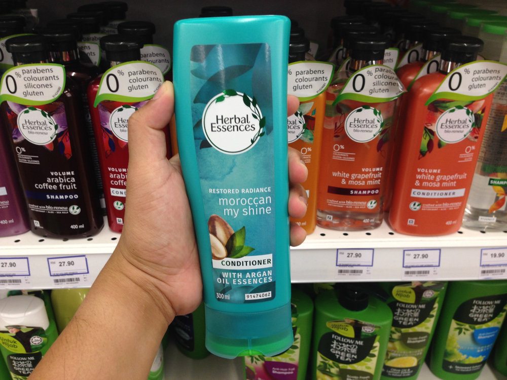 Persoon die een shampoofles vasthoudt met anderen op de achtergrond voor een stuk getiteld Is Herbal Essences Good for Your Hair