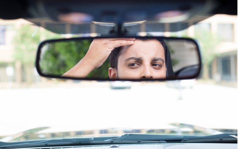 Als afbeelding voor de beste kapsels voor mannen met weduwe pieken, een man die naar zijn terugwijkende haarlijn kijkt in de autospiegel