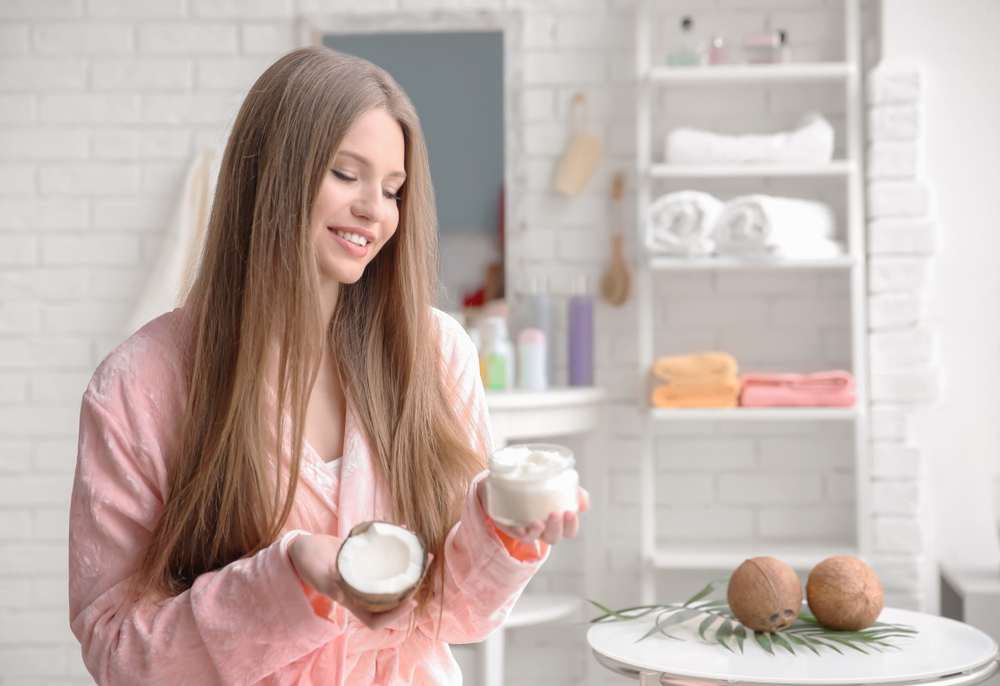 Vrouw gebruikt kokosolie voor het bleken van haar terwijl ze een kokosnoot en een pot van het spul vasthoudt