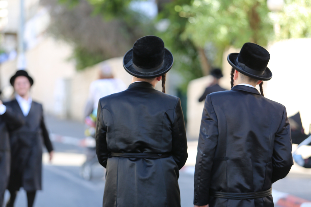 Twee joodse mannen met payots lopen langs een straat en praten terwijl ze hoeden dragen