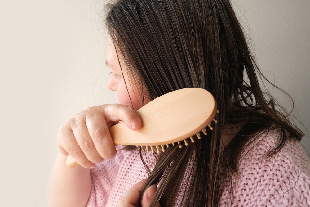 Vrouw met wasachtig haar die een houten borstel door de lokken haalt