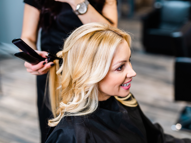 Haarstylist blondeert een vrouw in haar salonstoel