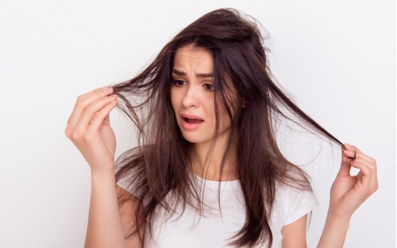 Om de vraag te beantwoorden wat is haar porositeit, een vrouw die in een witte kamer staat met haar beschadigde haar omdat ze onze gids niet heeft gelezen