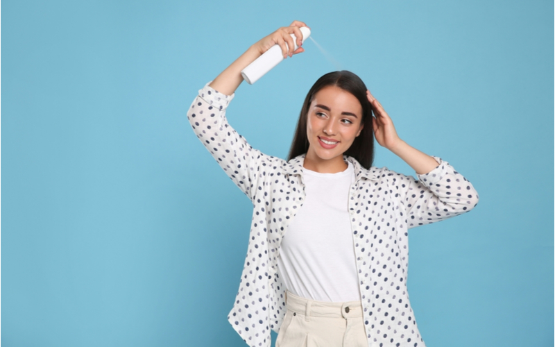 Vrouw gebruikt een droog shampoo alternatief op haar haar in een blauwe kamer