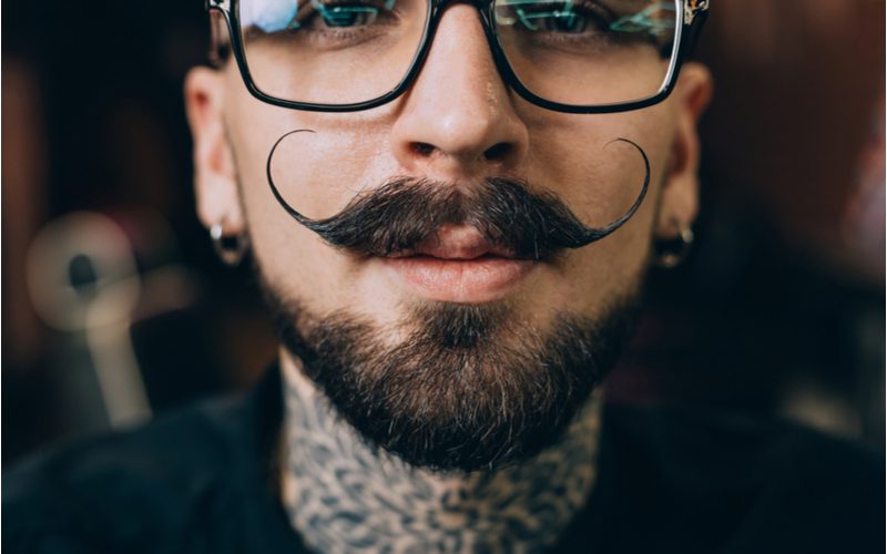 Gestileerde Verdi Type baard op een hipster man met donkere bril, een zwart shirt en met nek tatoeages