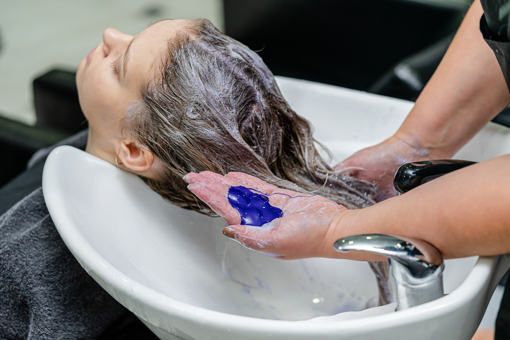 Vrouw gebruikt paarse shampoo in een salonstoel om haar haarkleur langer te laten duren