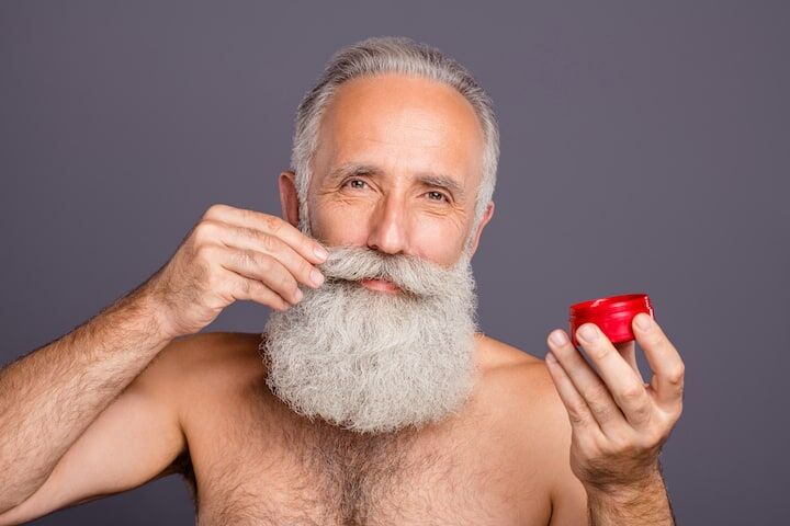 Oudere man met dikke grijze baard die pommade aanbrengt