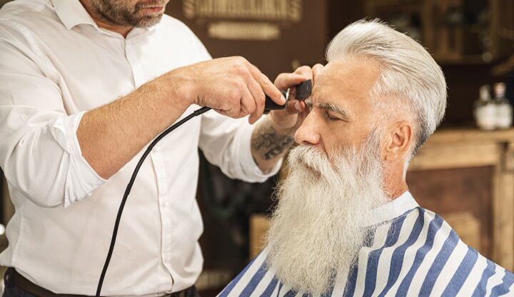 Man met lange witte baard laat zijn haar knippen