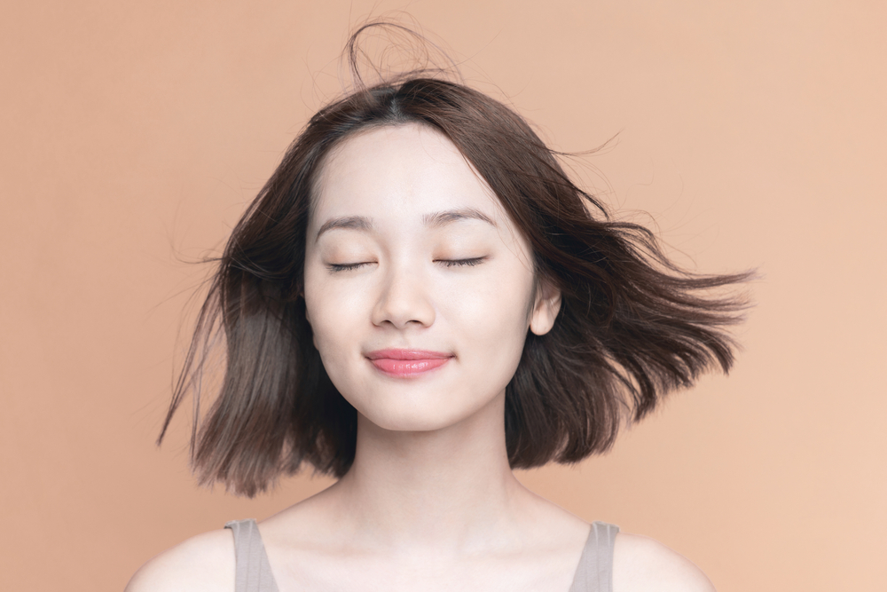 Vrouw sluit haar ogen en vraagt zich af kun je je haar wassen met alleen water terwijl ze haar haar laat wapperen in de wind