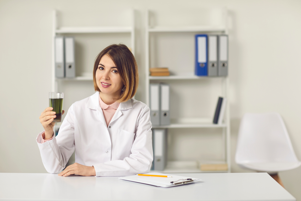 Voedingsdeskundige aan een bureau die een smoothie in een glas omhoog houdt om de voordelen van chlorofyl op haar te benadrukken