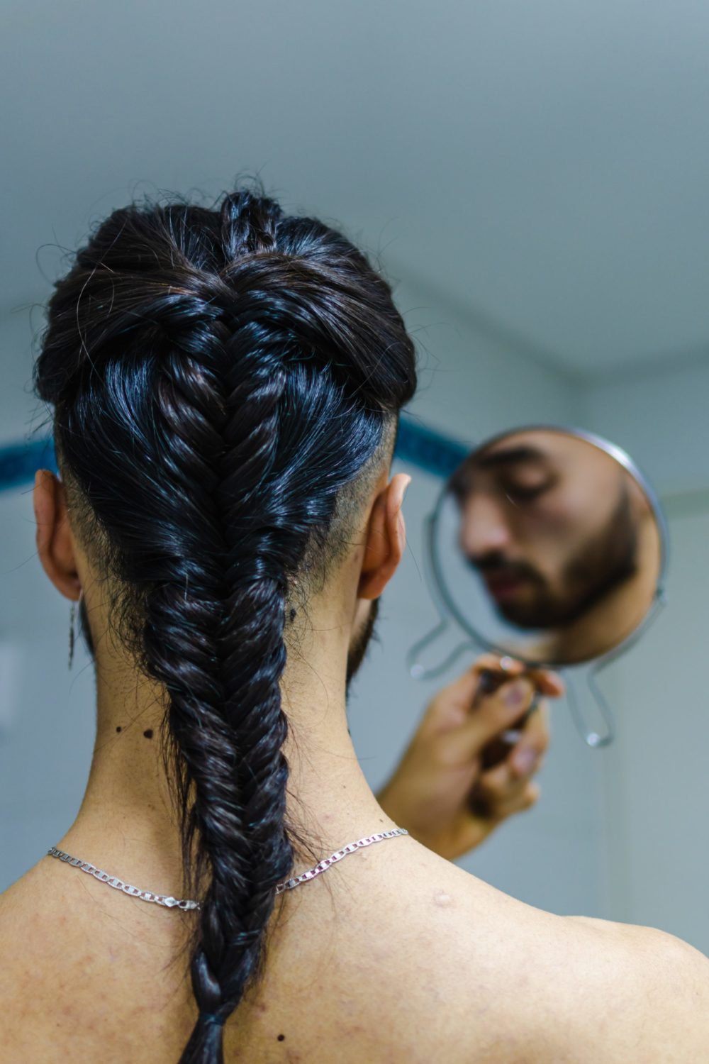 Twisted Fishtail White Mens Braid op een man die een spiegel tegen zijn voorhoofd houdt.