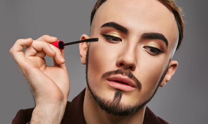 Trans man met baard die mascara aanbrengt