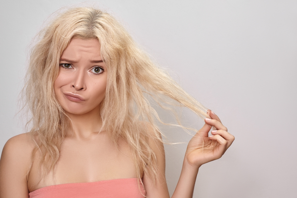 Prachtige vrouw met beschadigd gebleekt haar die haar lokken omhoog houdt