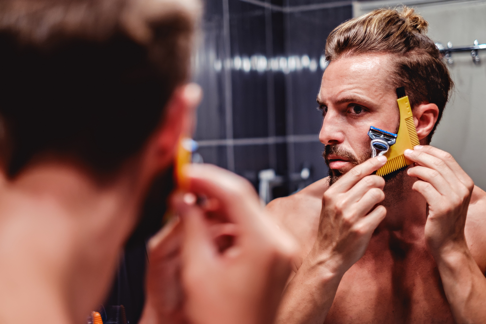 Man vormt zijn baard met een vormer terwijl hij in de spiegel kijkt