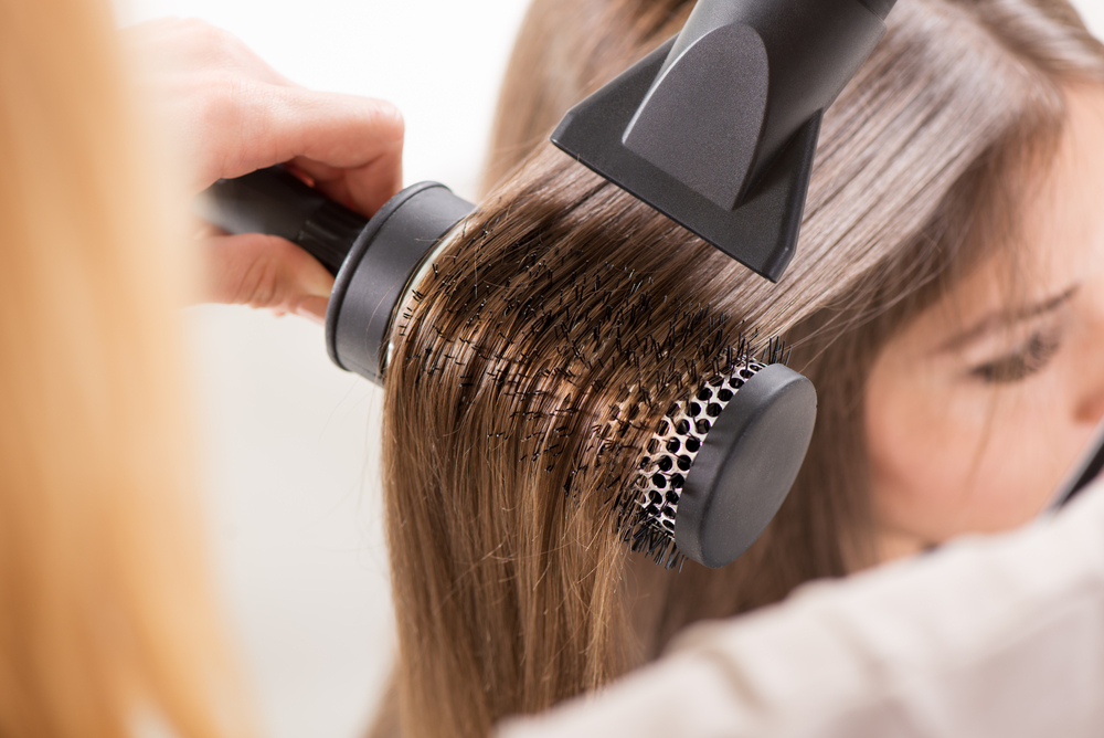 Vrouw die een haardroger gebruikt om haar haar recht te trekken samen met een ronde borstel