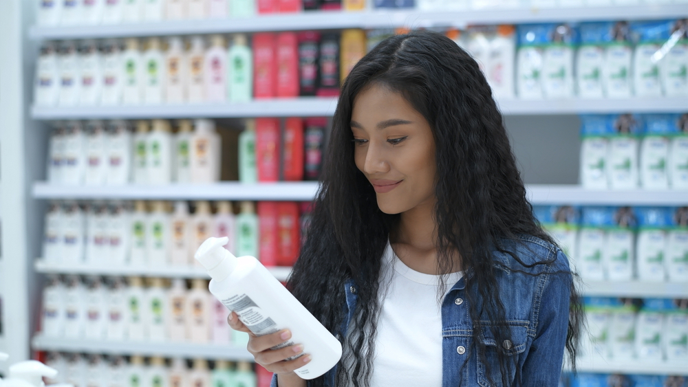 Vrouw kijkt naar de beste shampoo voor Aziatisch haar in een winkel terwijl ze een jeansjack draagt