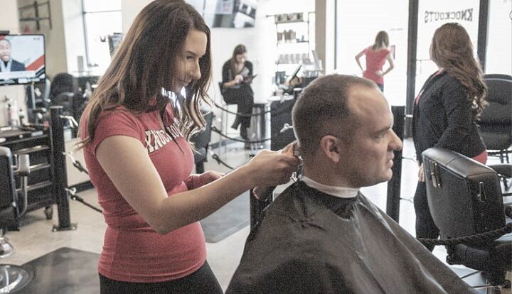 Vrouwelijke kapper die het haar van een man in een salon trimt