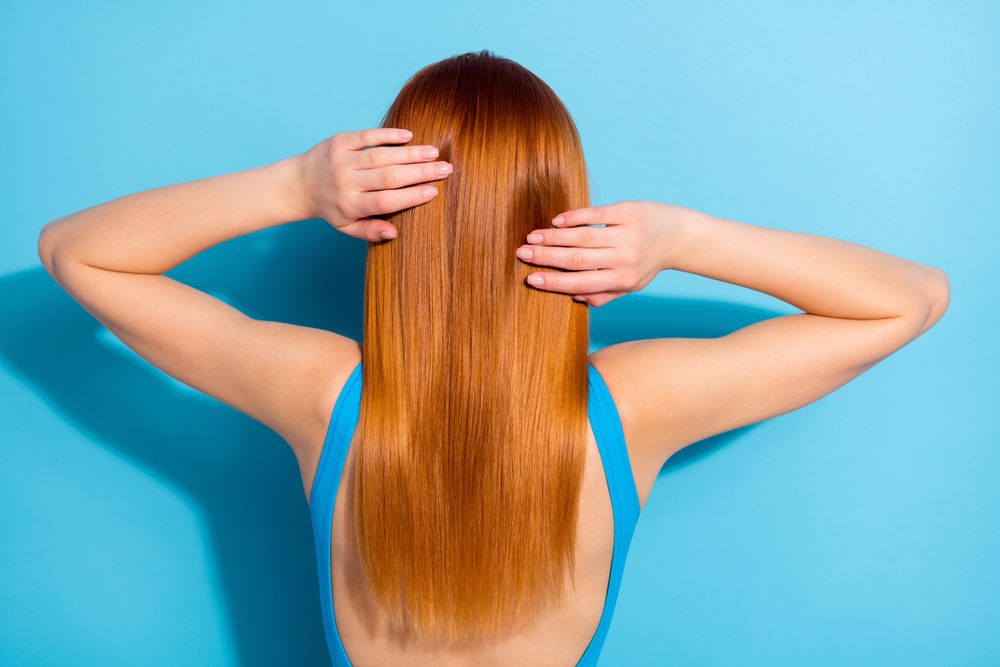 Licht koper, een van de beste haarkleuren voor rood haar op een vrouw in een blauw shirt die in een blauwe kamer staat.