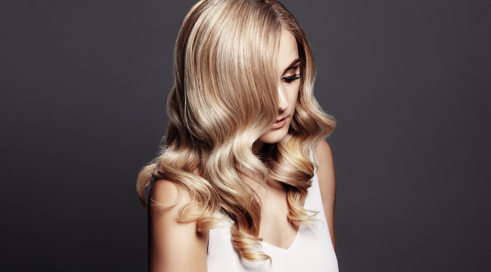 Vrouw kijkt neer op donkergrijze achtergrond met dimensionale honingblond als een van de beste haarkleur voor vuile blondines
