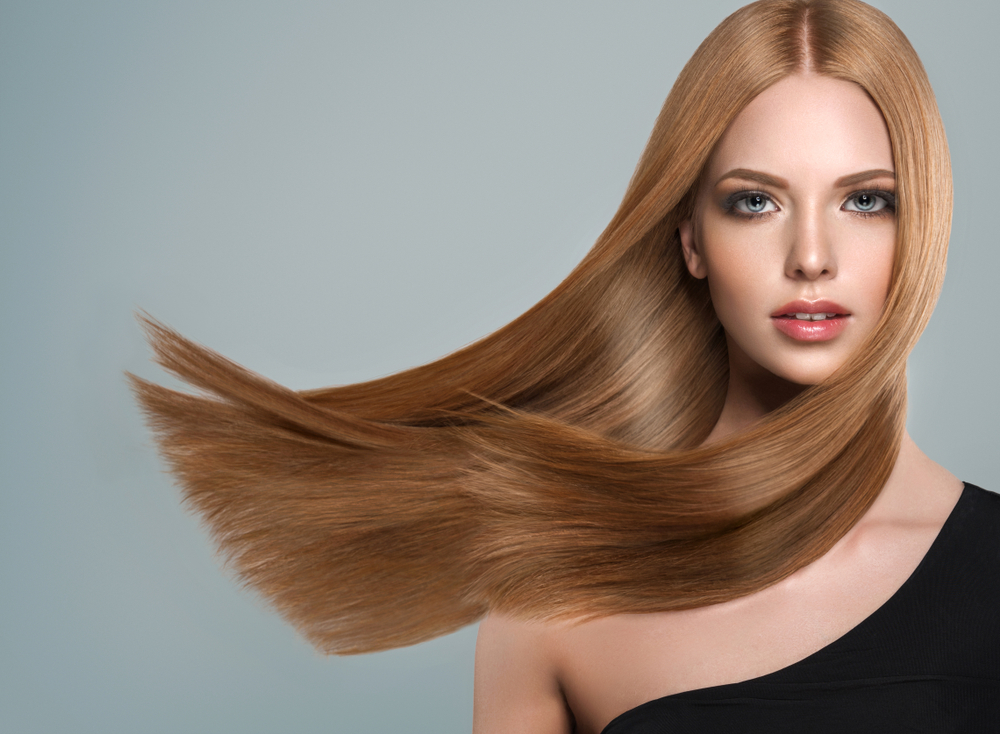 Vrouw kijkt naar camera met donkerblond haar dat waait in de wind