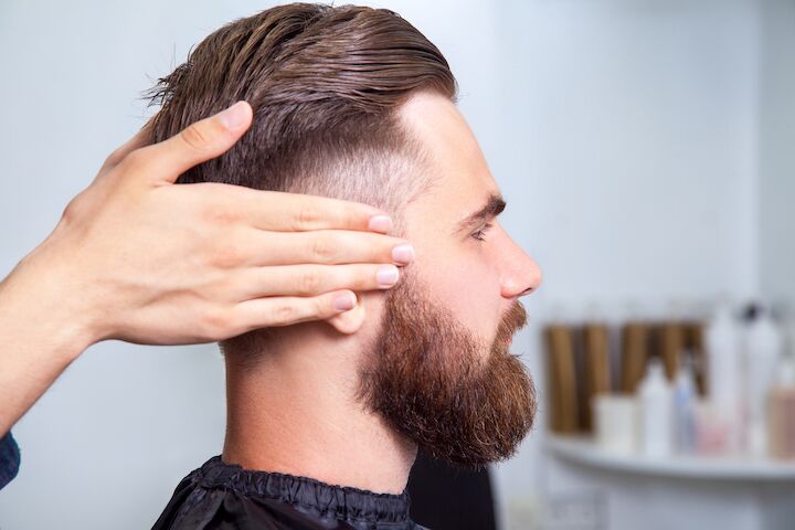 Man met baard en kapsel zittend in een kapperszaak