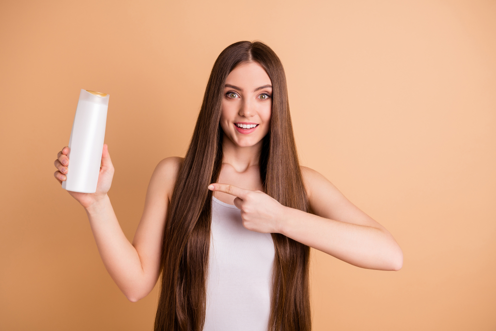 Vrouw houdt een fles van de beste kleurafgevende shampoo vast en wijst naar de fles