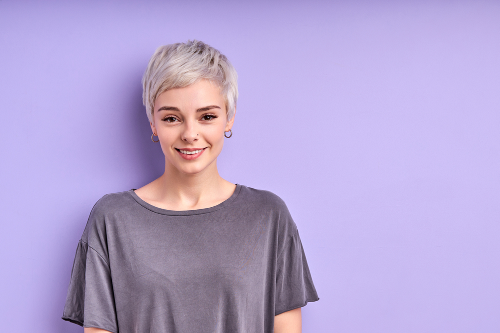 Vrouw met zilveren pixie die één van de beste haarkleur voor kort haar op lavendelachtergrond toont