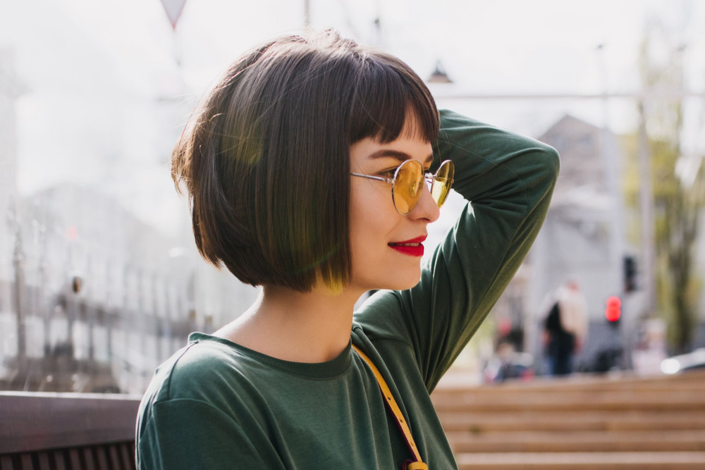 Vrouw met opgeheven arm kijkt uit op stadslandschap in espresso bruin haar om te pronken met een van de beste haarkleur voor kort haar