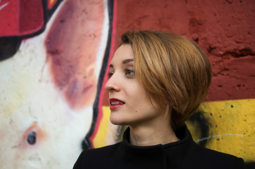 De vrouw voor geschilderde muur kijkt af met karamel donker blonde haarkleur voor kort haar