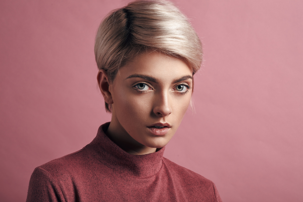 Vrouw met open mond voor roze muur ziet er recht uit met platina als een van de top haarkleuren voor kort haar