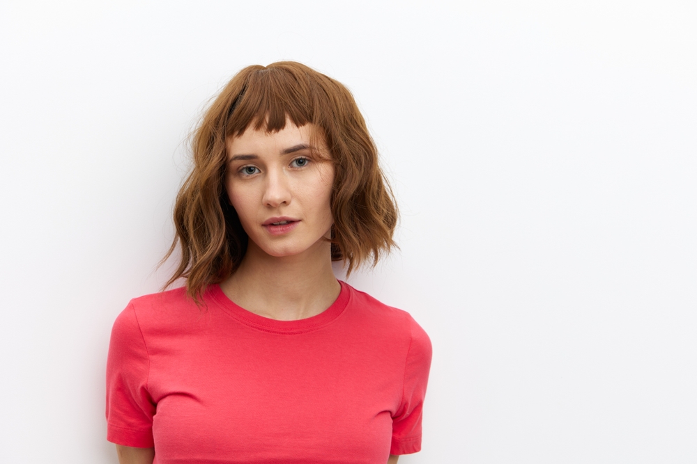 Vrouw staat tegen witte muur met roze shirt met kaneel als een van de beste haarkleur voor kort haar