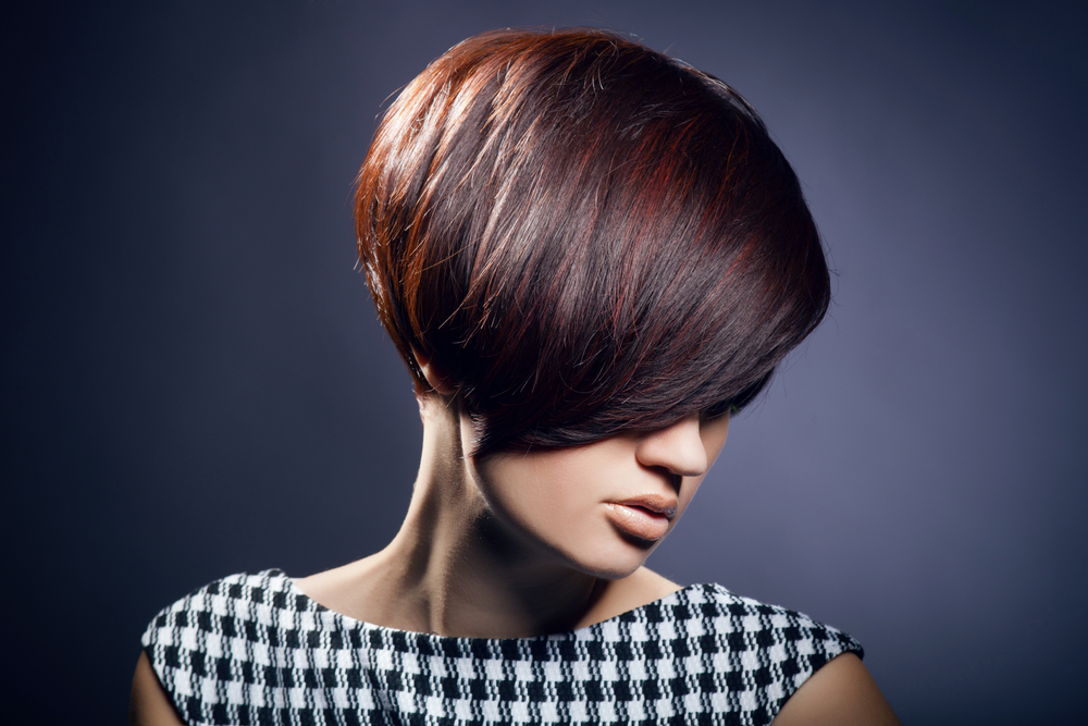 Serieuze vrouw kijkt naar beneden met de beste haarkleur voor kort haar gedrapeerd over haar oog in een jurk met ginghamprint