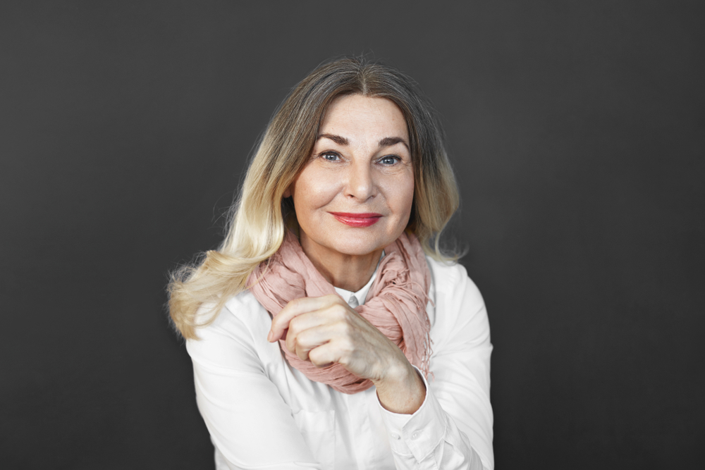 Volwassen vrouw op donkere achtergrond glimlacht het dragen van de beste haarkleur voor leeftijd met een blonde ombre