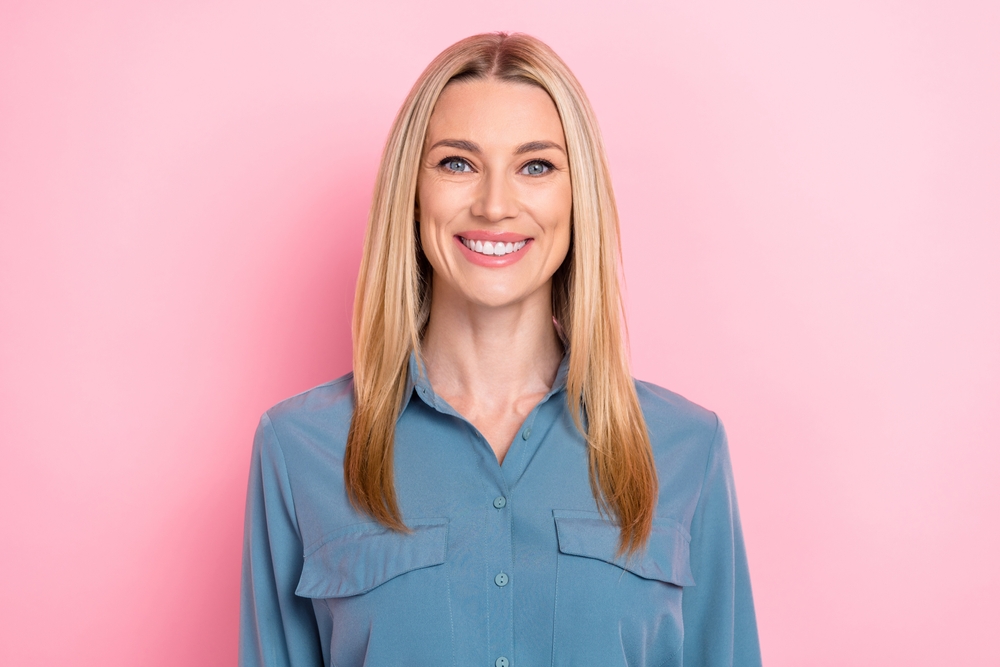 Vrouw van middelbare leeftijd ziet er jonger uit met de beste haarkleur voor leeftijdsomkering in gouden blonde ombre op roze achtergrond