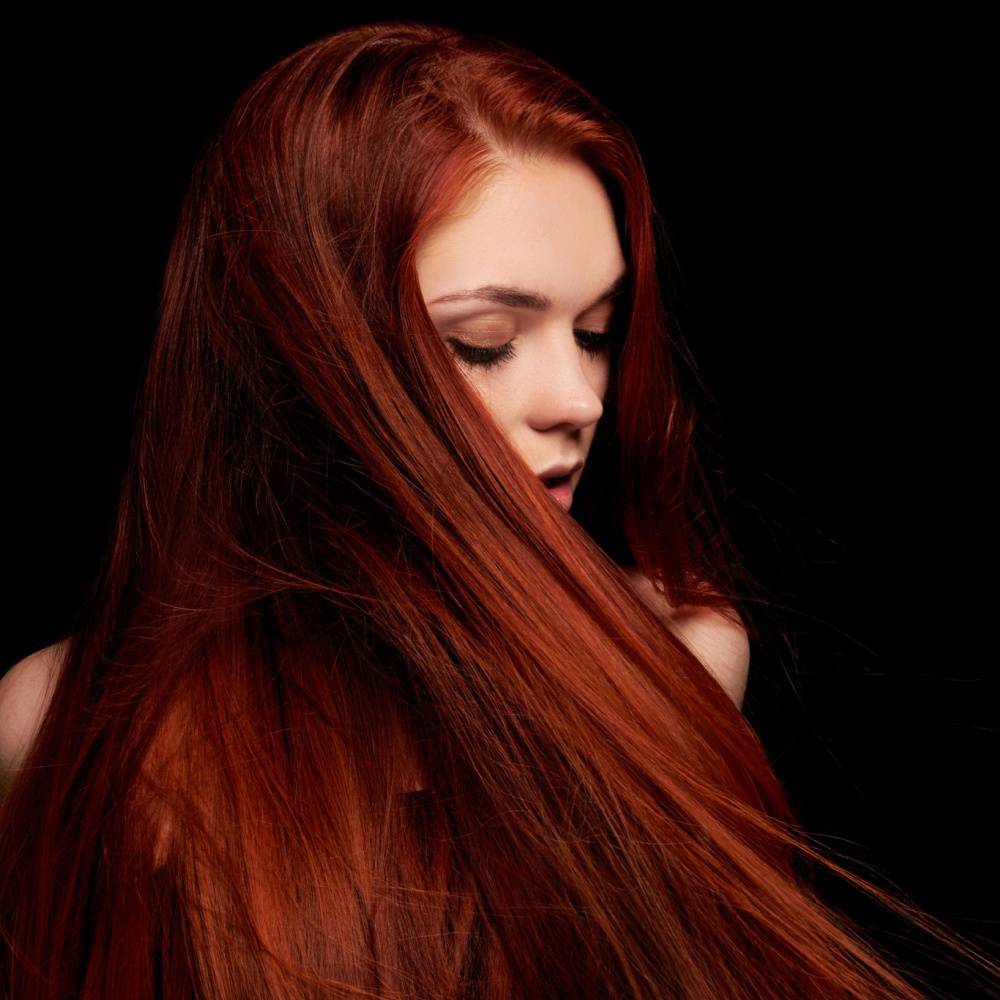 Vrouw in duisternis met lange rechte bloed oranje kleur pronkend met een van de beste warme rode haarkleuren