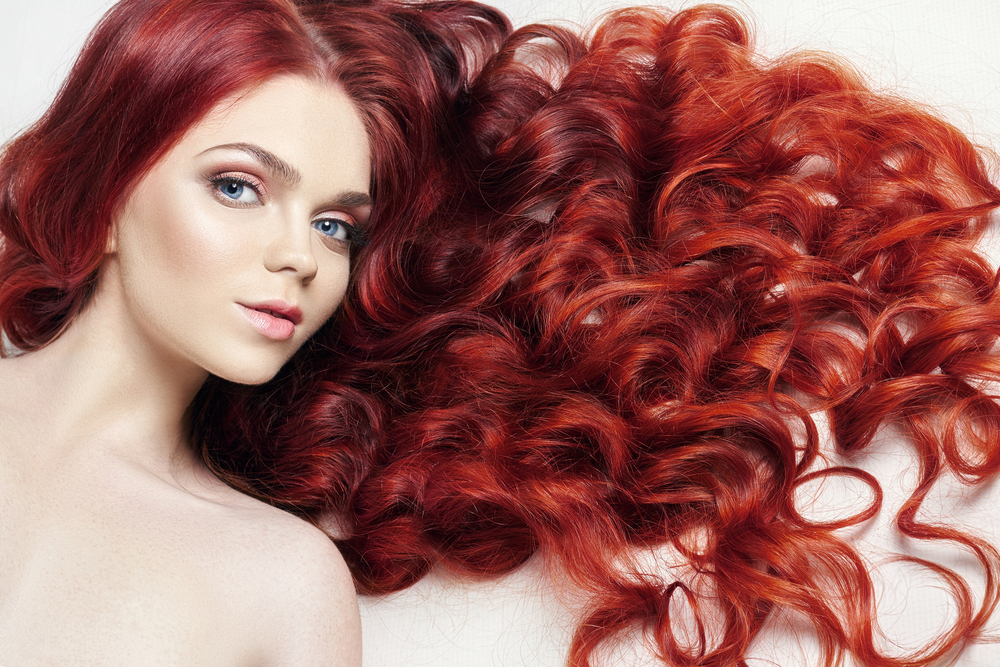 Vrouw ligt met krullend haar verspreid om haar heen op een wit vlak met een warme rode ombre haarkleur