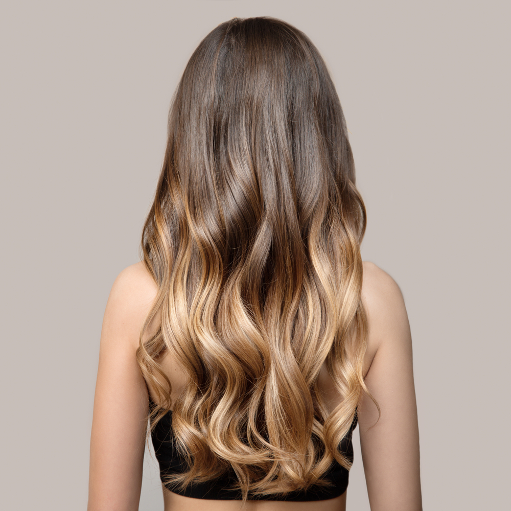 Achteraanzicht van vrouw met lang haar gestyled in losse golven met bruin tot blonde ombre kleur