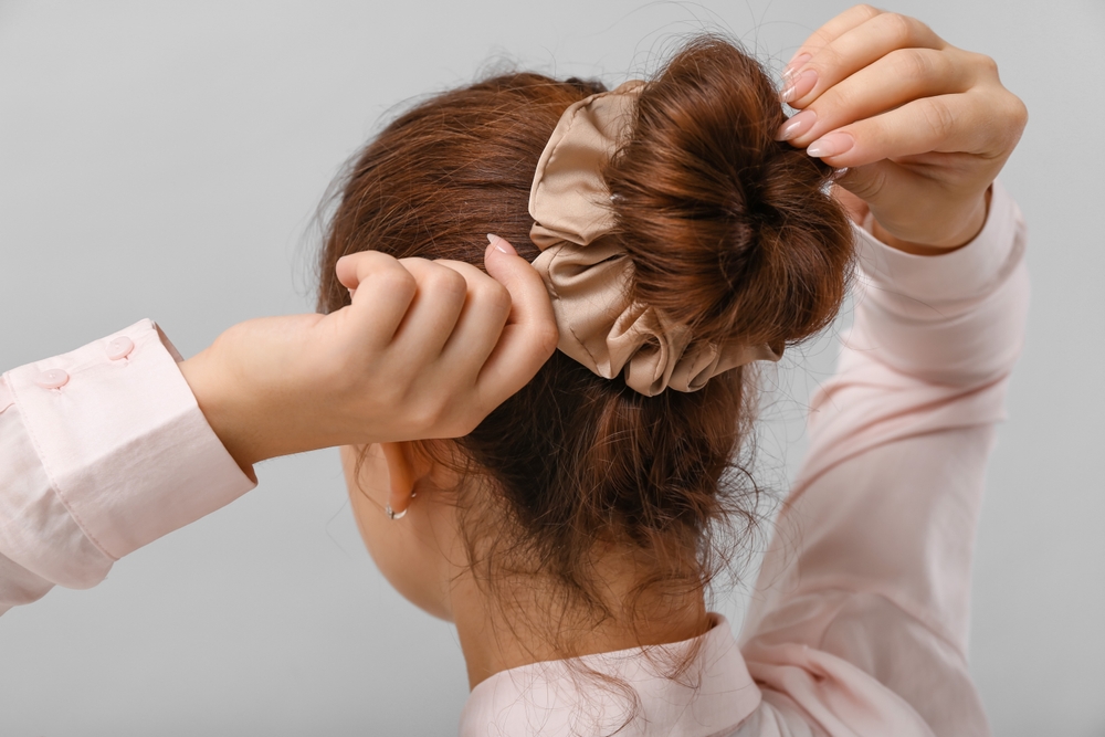 Achteraanzicht van vrouw met lange mouwen die haar haar in een scrunchy bun bindt als voorbeeld van een leuk kapsel voor lang haar.