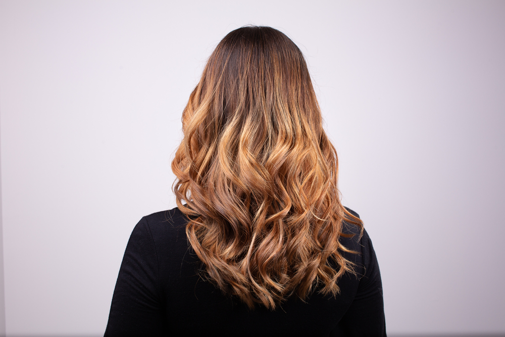 Achteraanzicht van vrouw met lang krullend haar in een honingblonde kleur gedaan met de balayage techniek