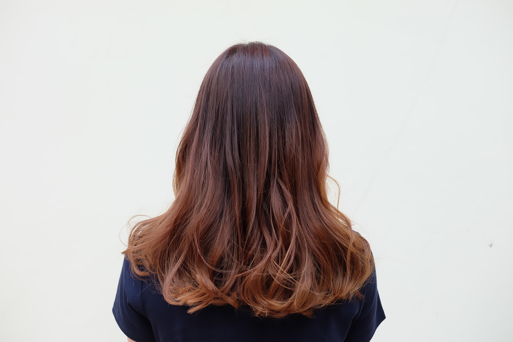 Achteraanzicht van vrouw met donkerbruin haar en auburn ombre kleur met zwart t-shirt voor gebroken witte muur.