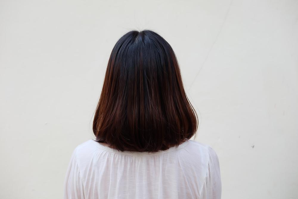 Achteraanzicht van vrouw in witte blouse met lang bobkapsel in donkerbruine tint met zwart