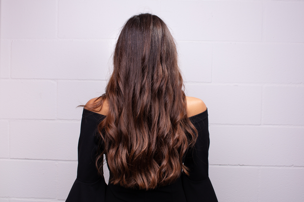 Achteraanzicht van vrouw die een off-shoulder zwart topje draagt met lang haar met donkerbruine en auburn balayage