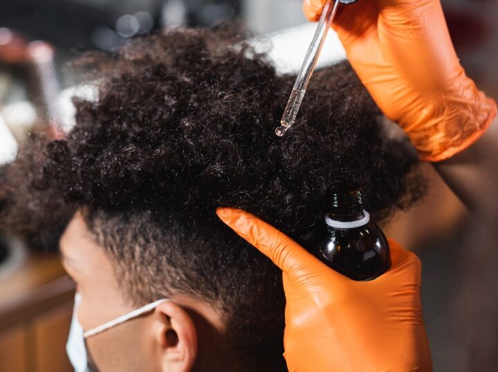 Haarolie aanbrengen op grof krullend haar van zwarte man