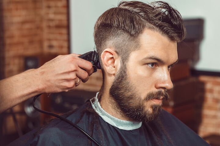 Kapper die elektrische trimmer gebruikt om het haar van de man te knippen