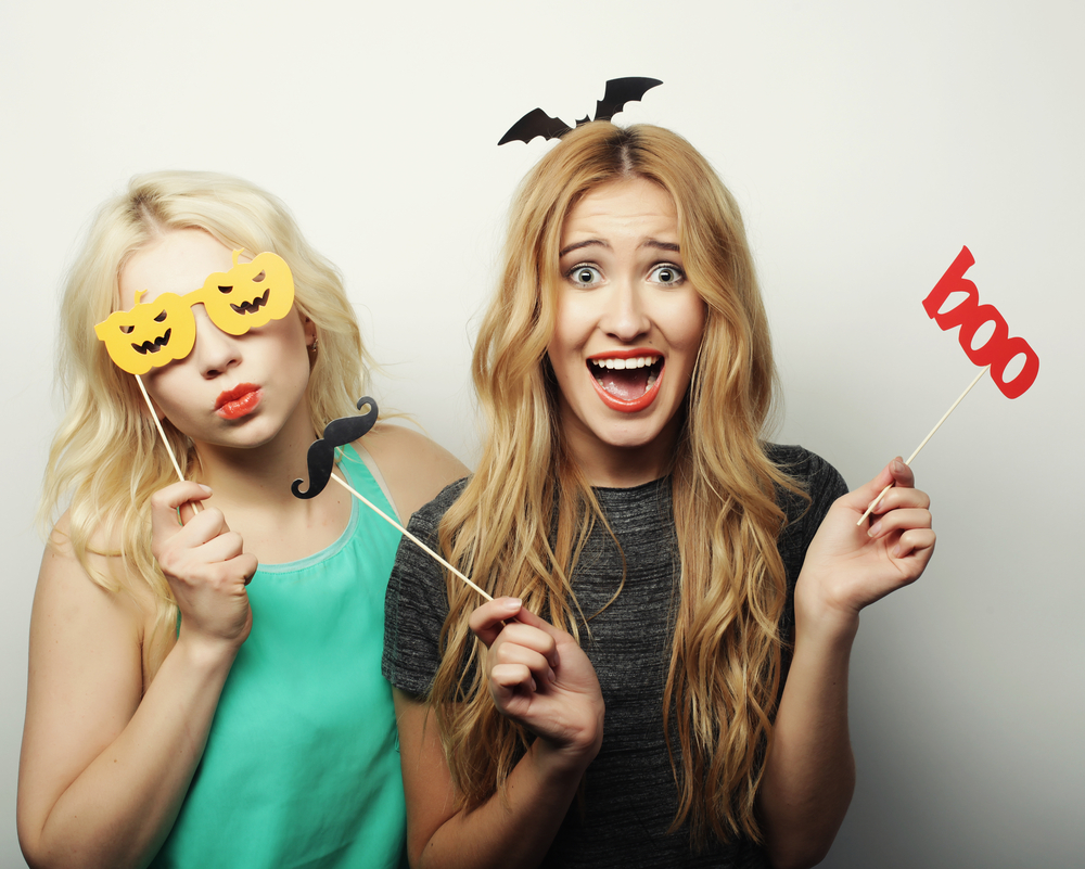 Twee blonde vrouwen tonen hun ideeën voor de beste Halloween kostuums voor blondines terwijl ze zich verkleden in een fotohokje