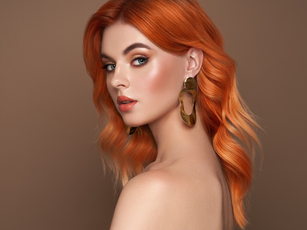 Vrouw met blote schouders en oranje koperen haarkleur pronkt met medium strandgolven kapsel in een losse halve bocht look