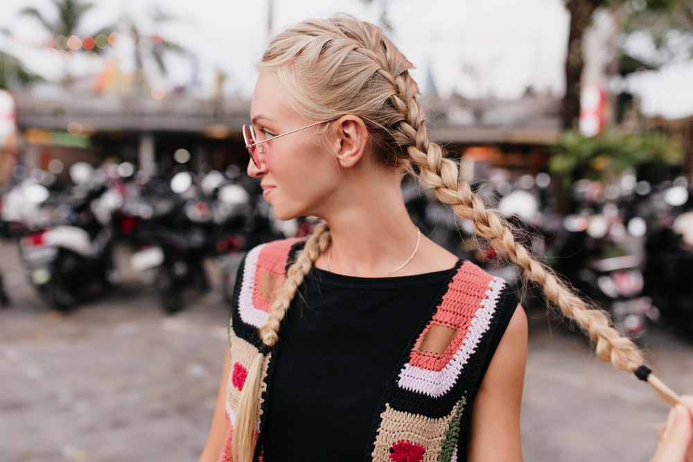 Vrouw in mouwloos gebreid vest met patroon toont één van haar favoriete kapsels voor dun haar met dubbele Franse vlechten.