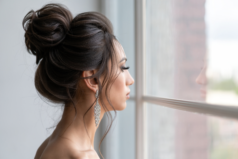 Vrouw staart uit het raam met formeel voorbeeld van kapsels voor lang dun haar in een volumineuze knot met bungelende fonkelende oorbellen