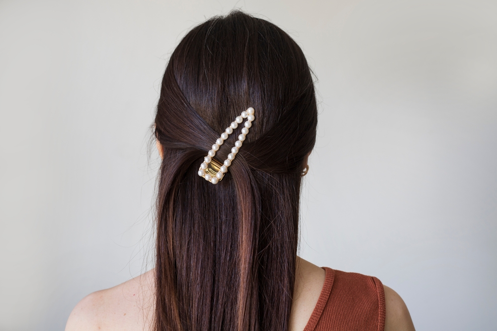 Achteraanzicht van vrouw in one-shoulder jurk voor grijze muur met een half-updo met behulp van een grote parel haarklem