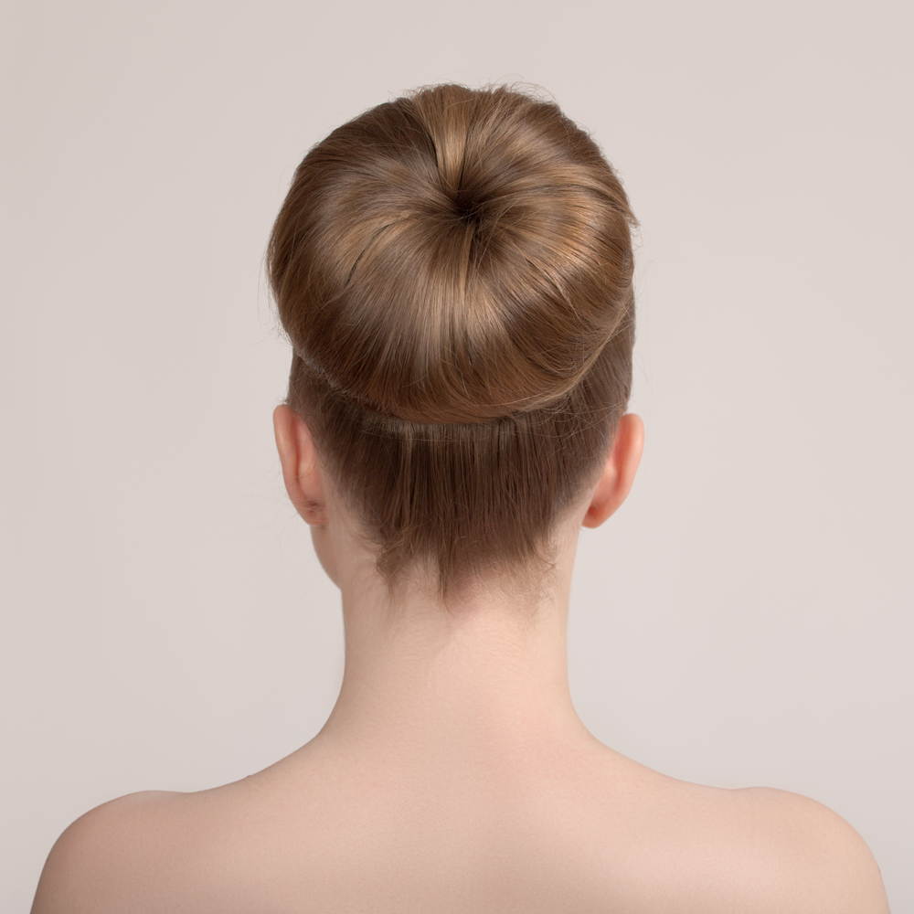 achteraanzicht van vrouw met blote schouders die een dikke ballerinaknot draagt met een haardonut voor lang dun haar